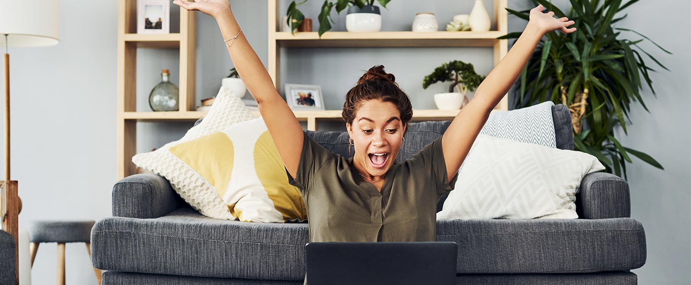 iStock-1165117030 Lady celbrating with arms up looking at laptop screen